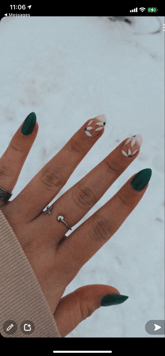 Fingernails with jewel green polish and two accent nails with clear polish and white leaf designs