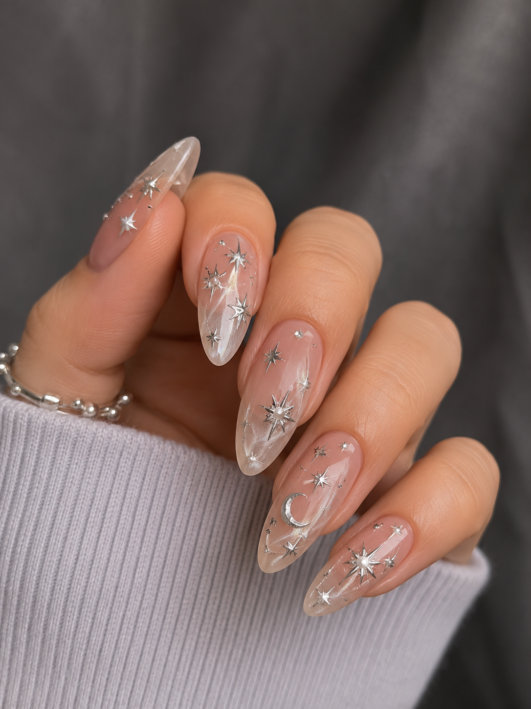 Close up of a hand with clear almond-shaped nails adorned with various sizes of silver star and moon designs.