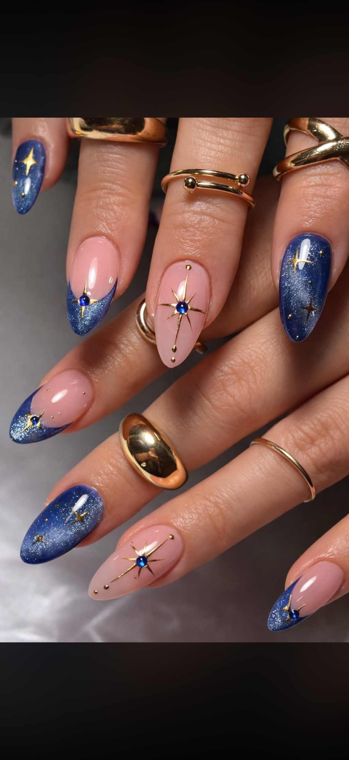 Almond-shaped nails with blue glitter tips with star decals, and nude nails with gold star decals and blue gem centers.