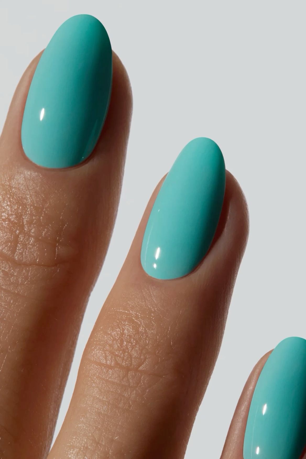 Close-up of a hand with several fingers showing oval-shaped nails painted in a solid, glossy, bright aqua polish.