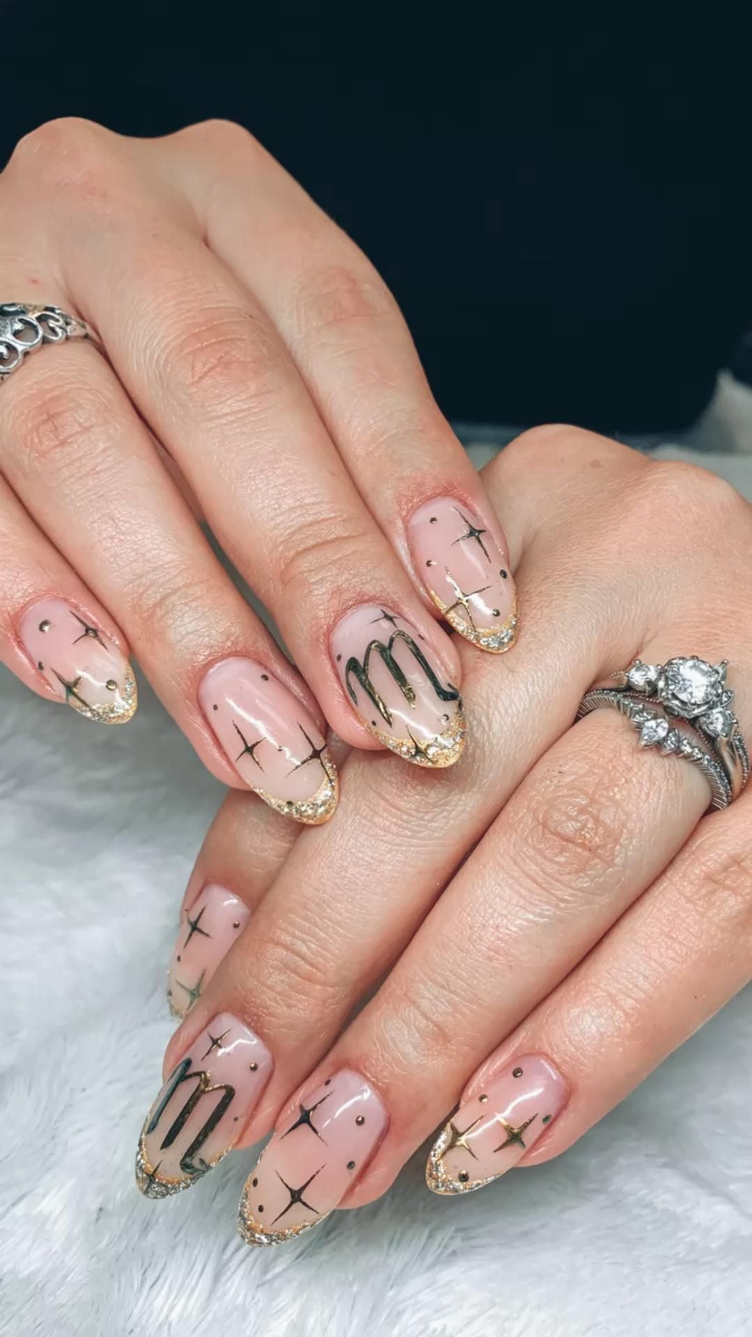 Close-up of manicured hands with almond-shaped nails featuring a Scorpio symbol on the middle finger and star designs.
