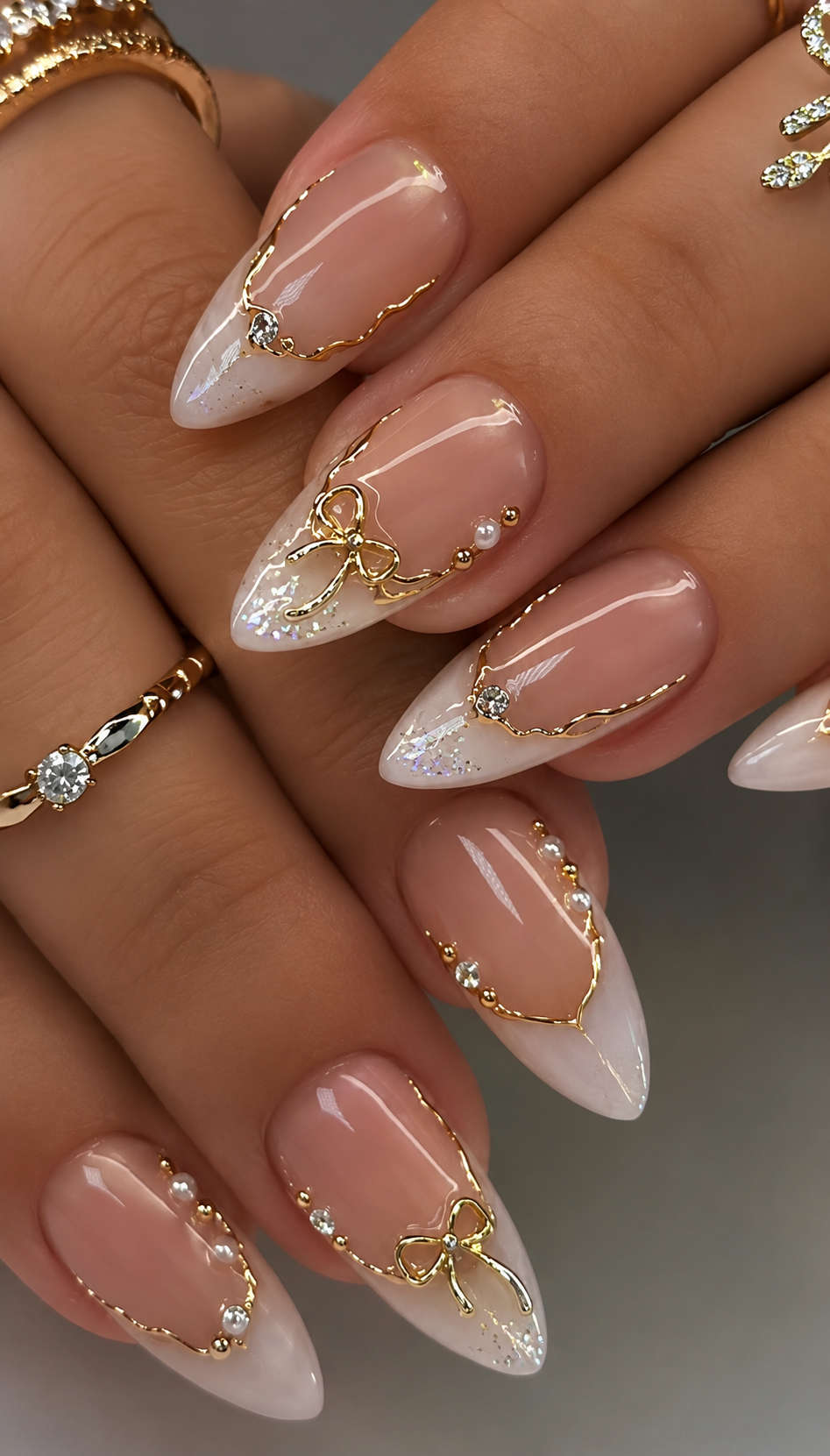 Almond-shaped nails feature beige and white tips, with gold embellishments and bows on each nail.