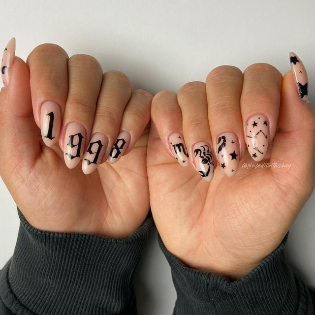 Manicured hands displaying almond-shaped nails, some with the numbers 1998 in a gothic font, others with star constellations…