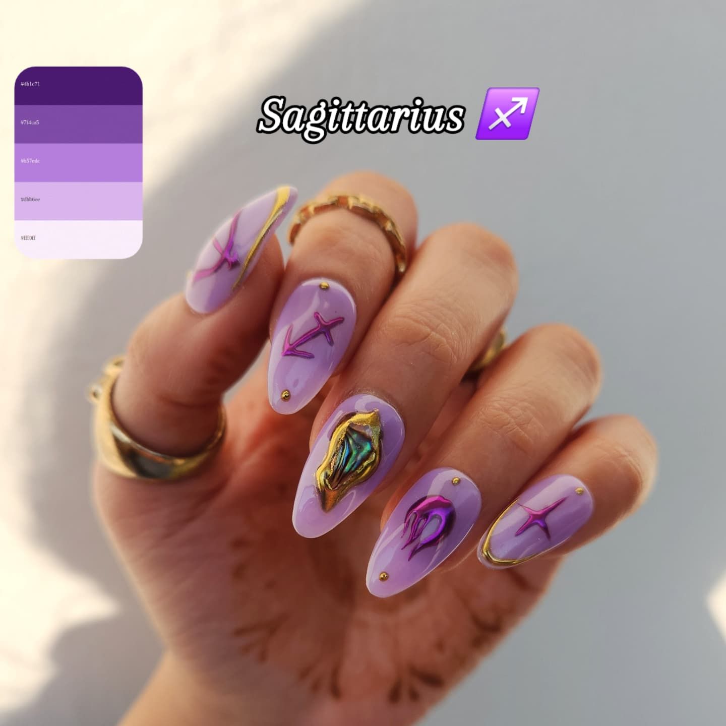 Pointed oval nails in a light purple with gold accents and raised chrome Sagittarius symbols and iridescent designs.