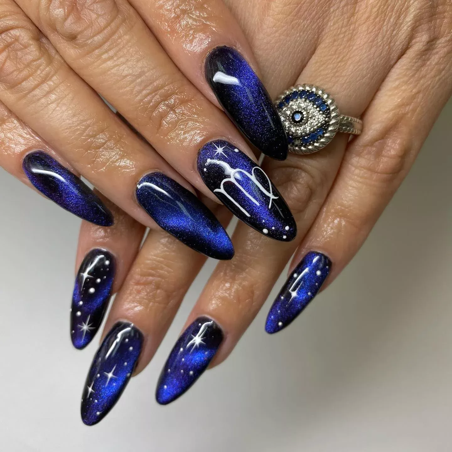 Close-up of nails with a blue-black gradient, scattered white dots, shining stars, and a white Virgo astrological symbol.