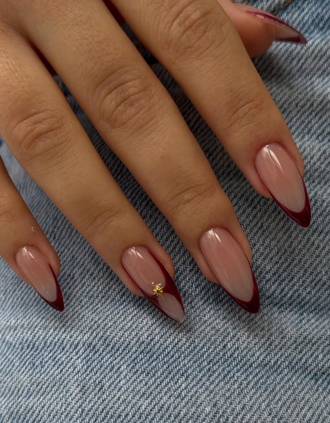 Pointed oval nails with deep maroon French tips, one nail adorned with a tiny gold star.
