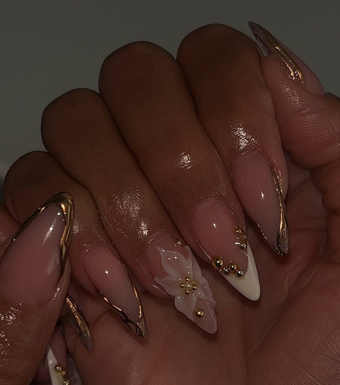 Close-up of a hand with long, almond-shaped nails featuring white French tips outlined in gold chrome, with additional gold…
