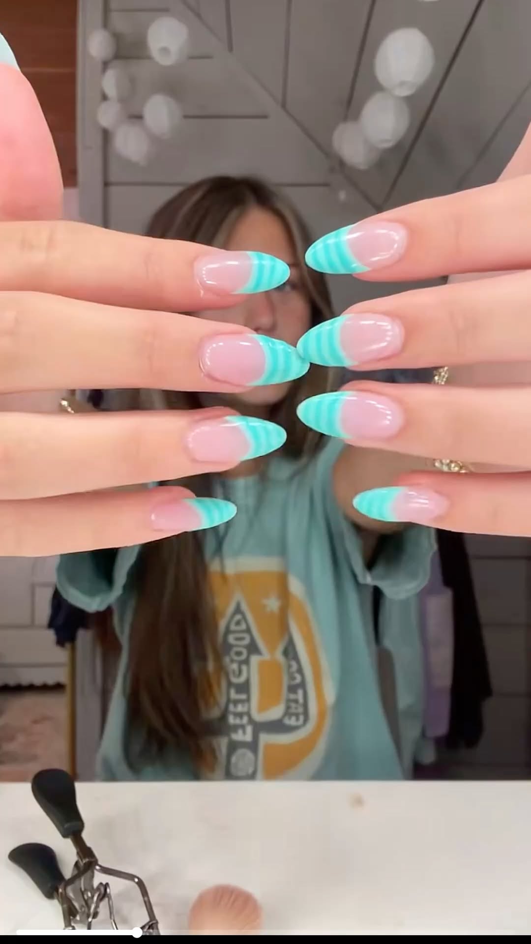 Pointed oval clear nails with aqua blue striped tips over a blurred background.