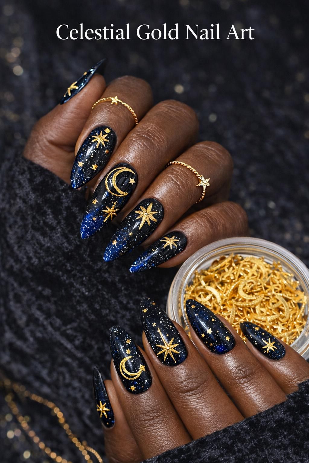 Close-up of manicured hands with dark blue and black nails, decorated with gold cosmic shapes like moons and stars.