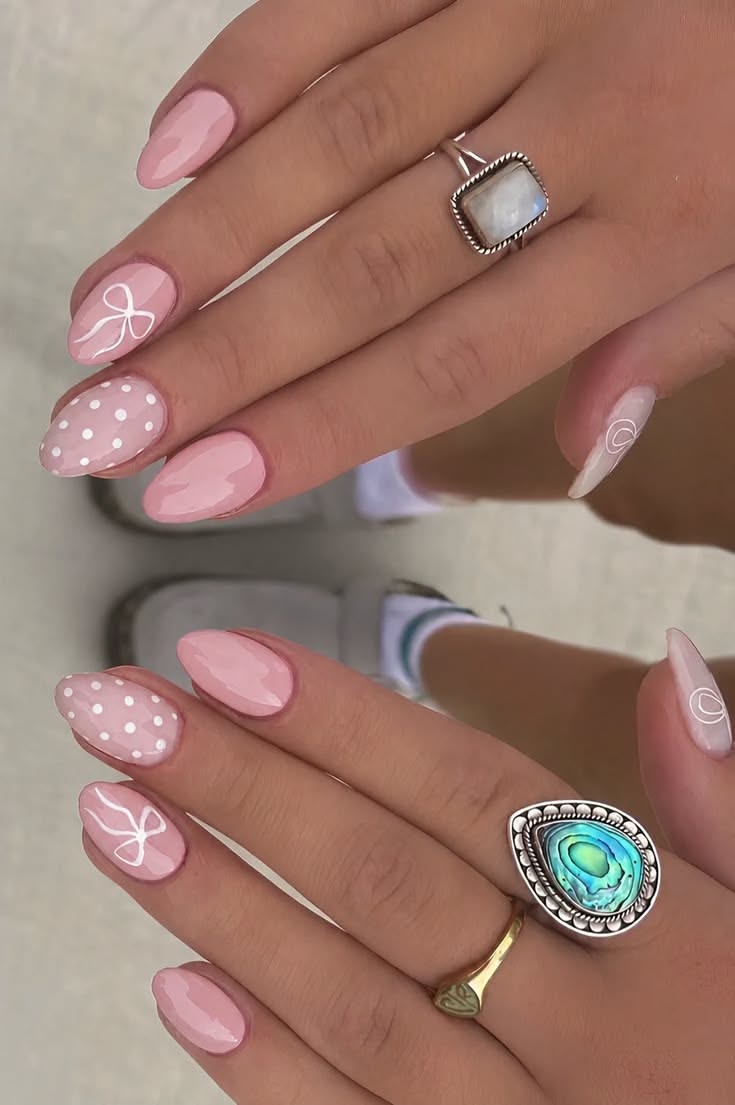 Close-up of manicured hands with light pink nails, some featuring white polka dots and others a white bow design.