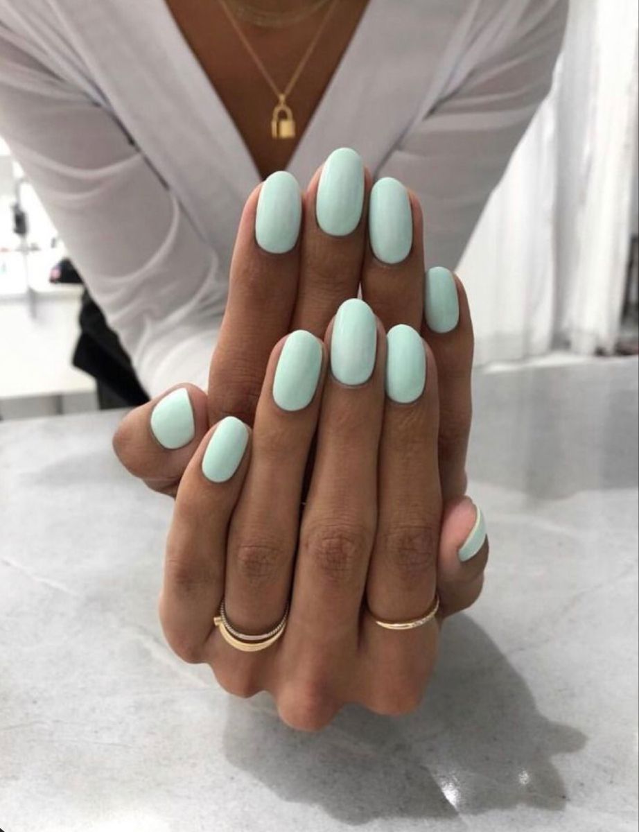 Hands with short, oval-shaped nails painted in a solid light aqua color.