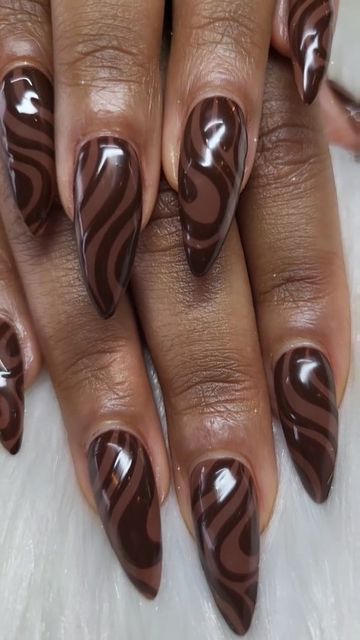 Close-up of a hand with long, glossy coffin-shaped nails featuring a dark and light brown swirl pattern.