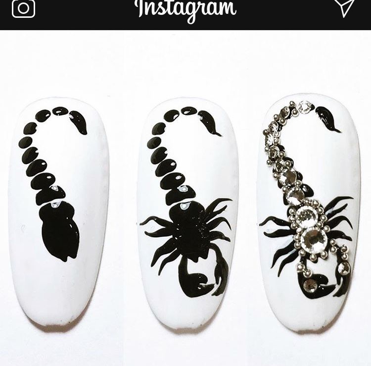 Three white artificial nails with increasingly elaborate black scorpion designs, the third featuring rhinestones.