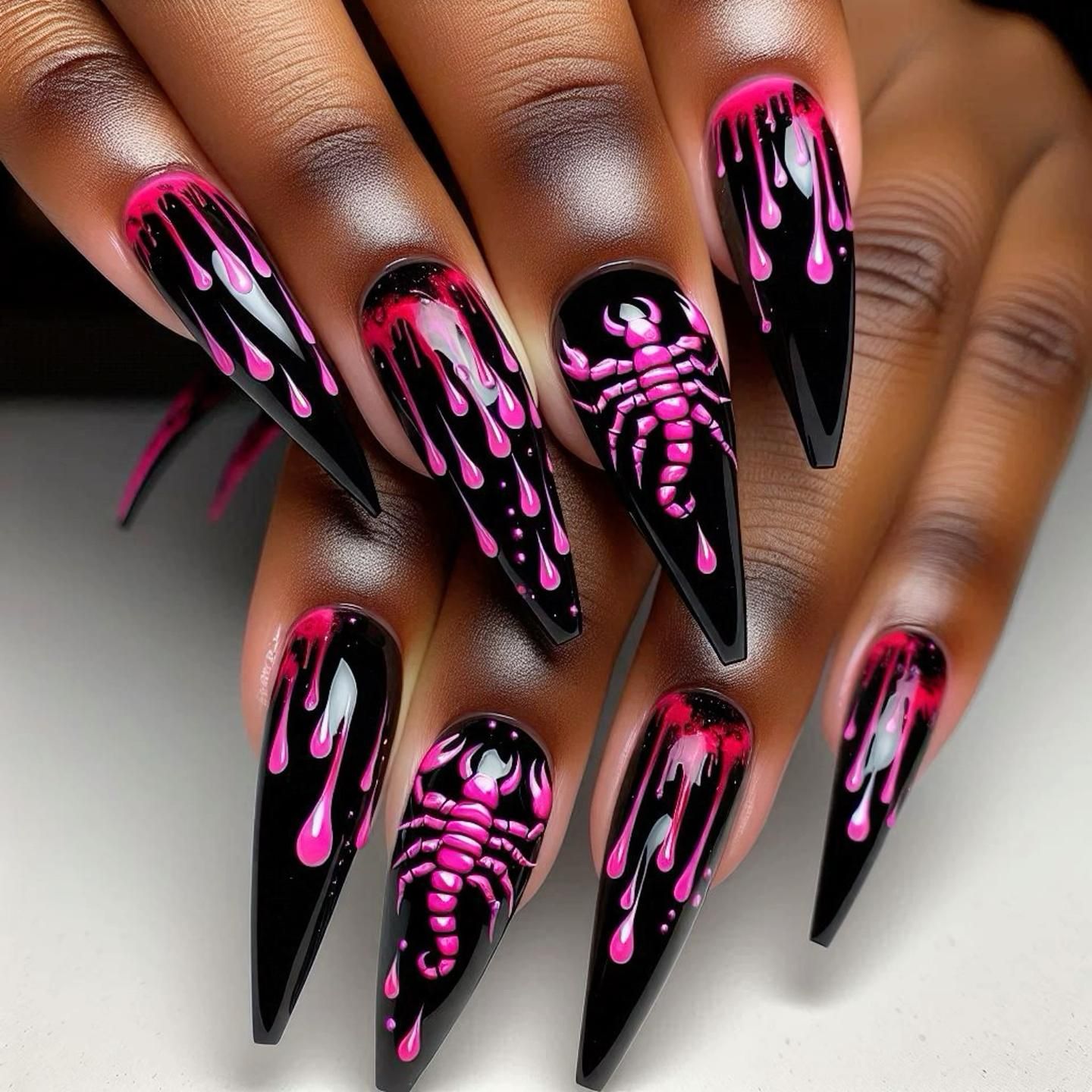 Pointed black nails with pink dripping paint and a neon pink scorpion design on two nails.