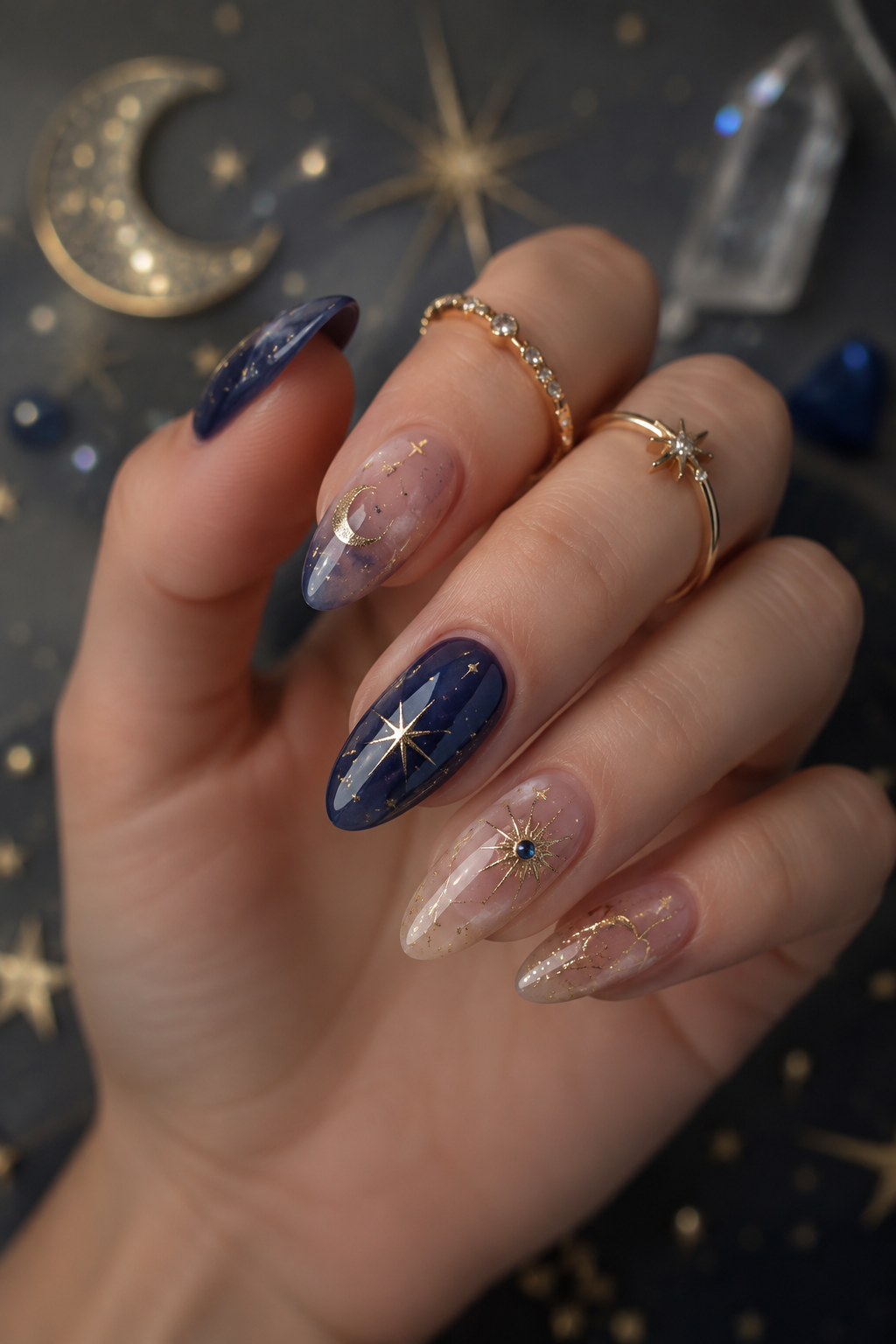 Close up of a hand with celestial-themed almond shape nails. Designs include gold moons, stars, and abstract swirls on a mix…