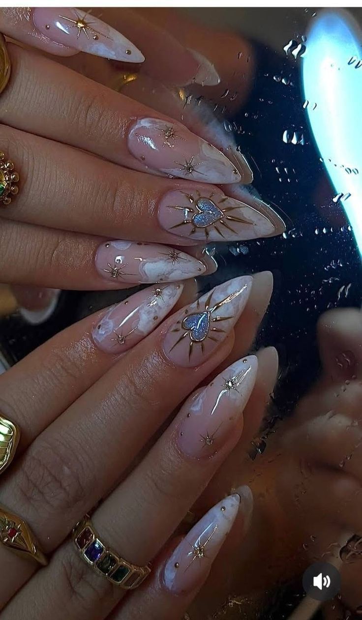 Close-up of a person's hands with long stiletto nails. The nails are decorated with small golden stars, dots, and iridescent…