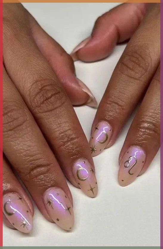Close-up of manicured hands with almond-shaped nails featuring iridescent polish and gold celestial designs like stars…