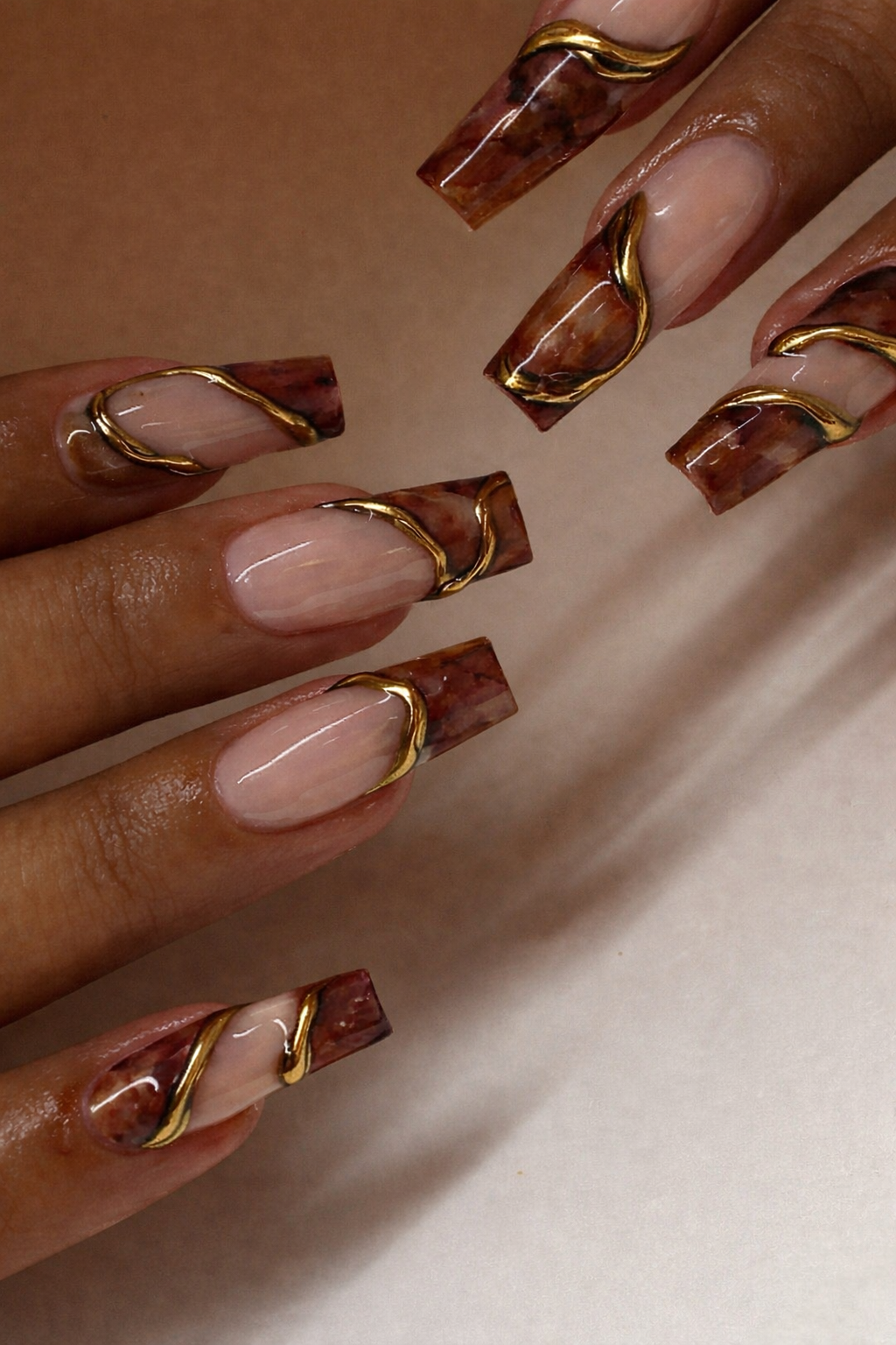 Close-up of coffin nails with a brown marble design and sculpted gold accents over a natural base.