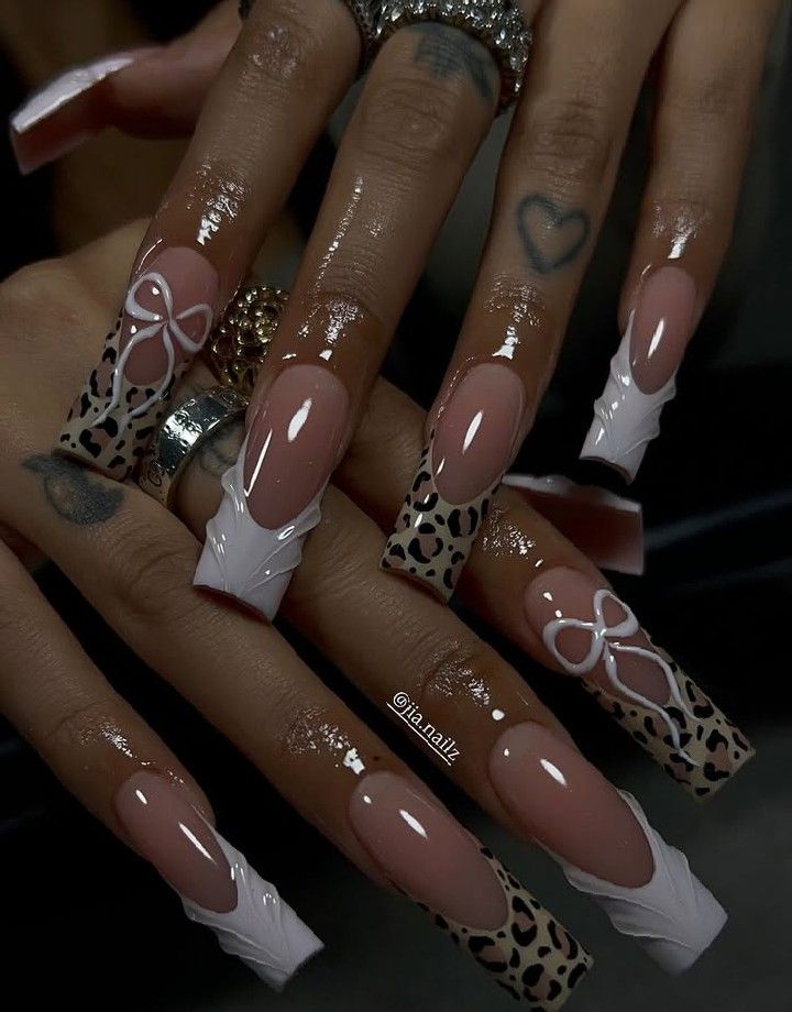 Close-up of extended almond-shaped nails featuring a French tip, some with leopard print, and some with white bow designs.