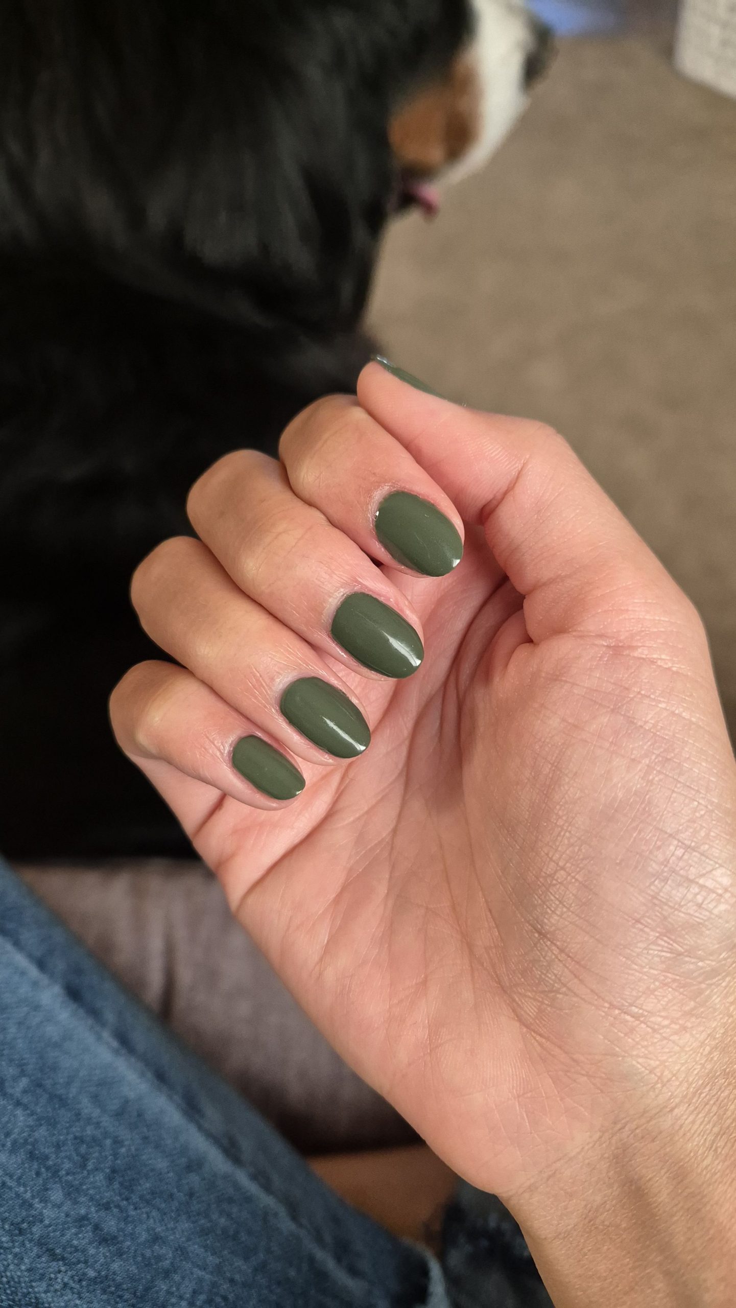 A hand with oval-shaped nails painted in a solid, glossy military green polish.