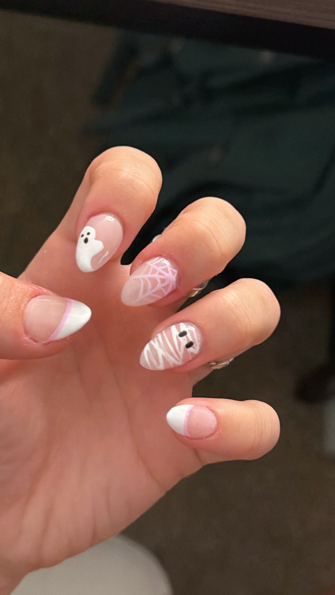A hand with short, almond-shaped nails featuring various Halloween designs.