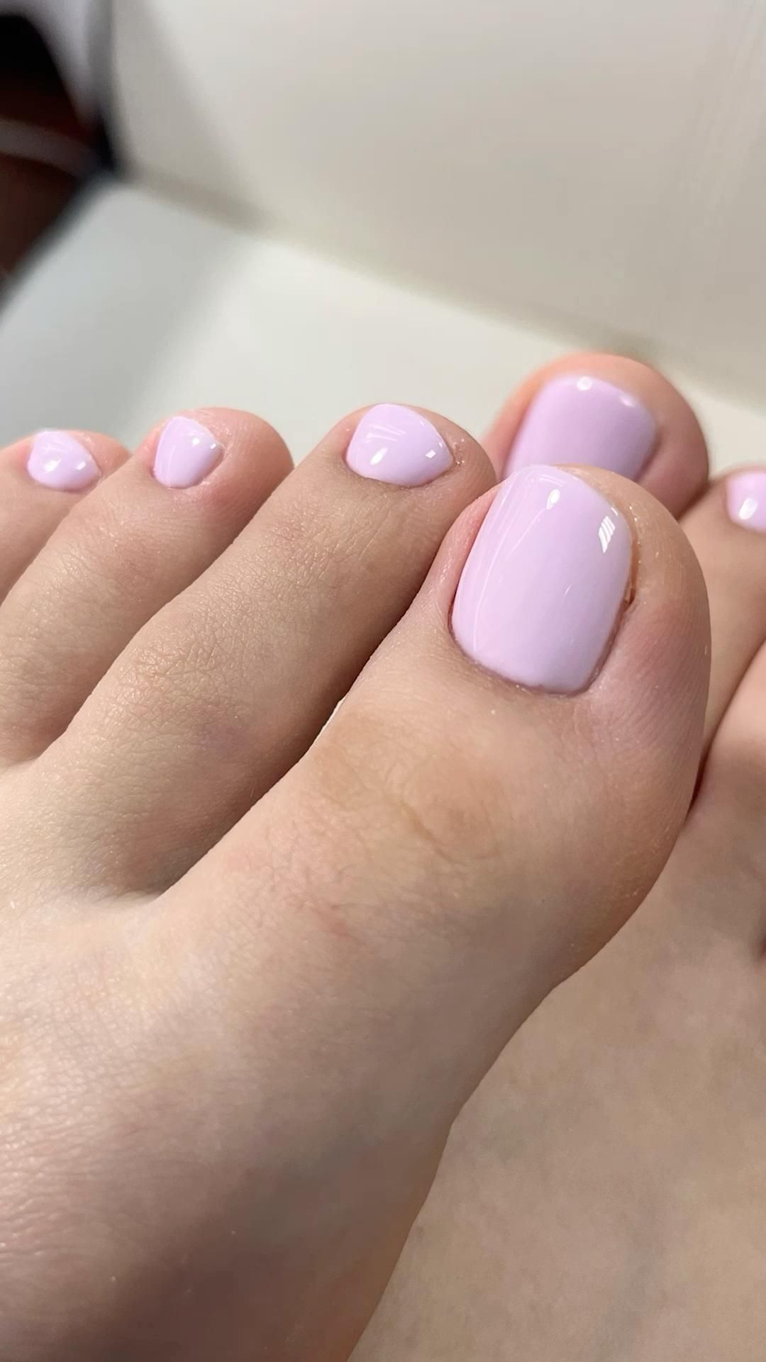 A close-up view of five toes with a light lavender-pink polish. The nails have a glossy finish and appear neatly manicured.