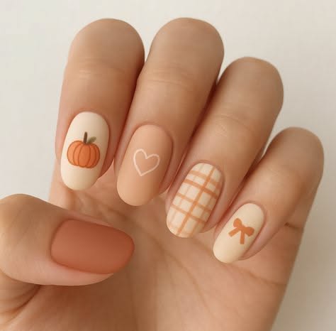 Close-up of a hand with short, round nails. Designs include a small pumpkin, a white heart outline, orange plaid, and an…