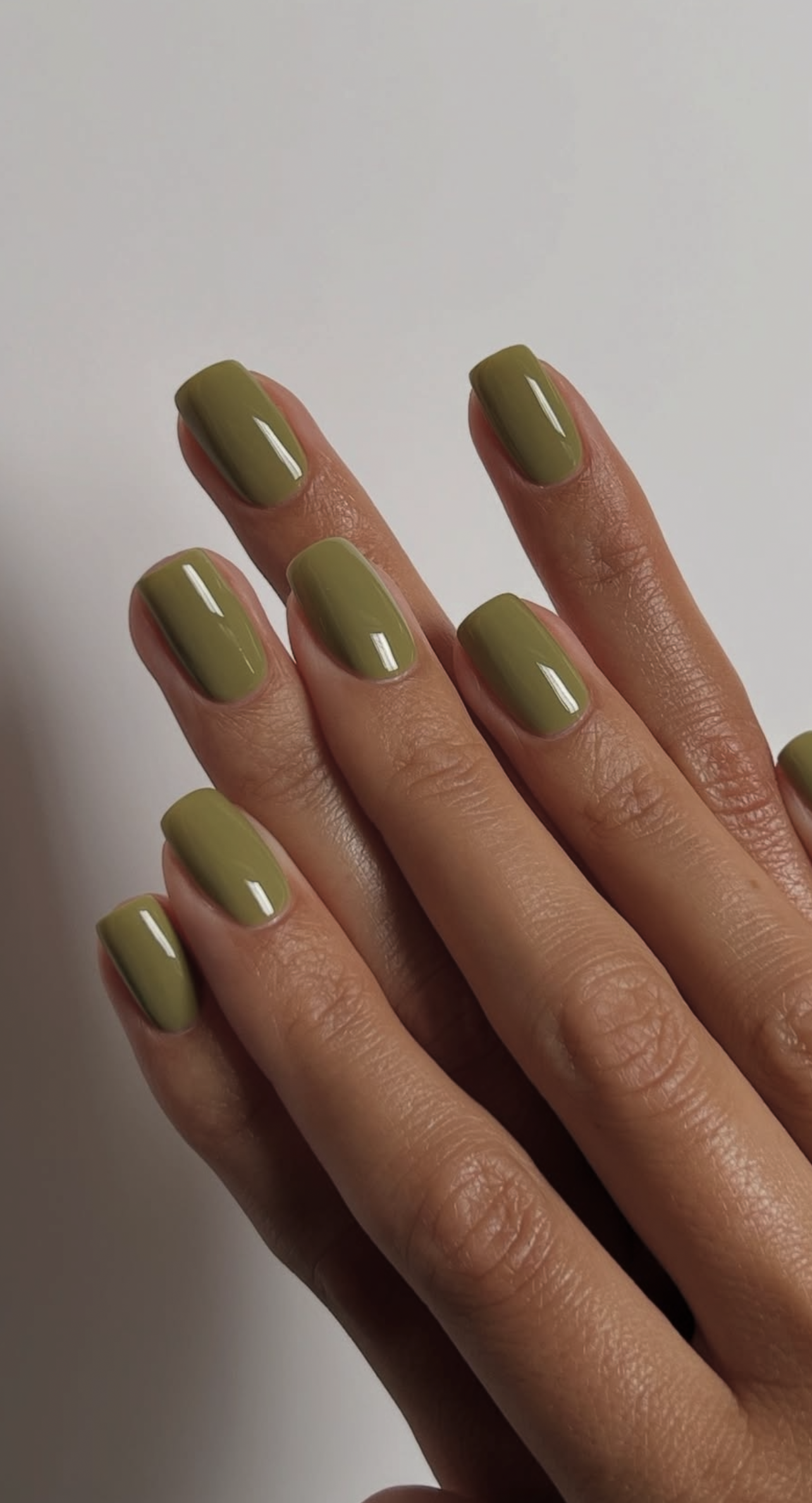 Close-up of a hand with nails painted a solid, glossy olive green color.