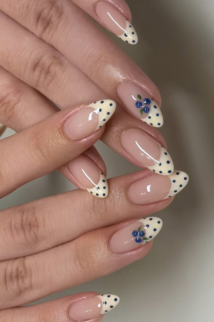 Almond-shaped nails with light pink base. Some nails feature French tips with white and blue polka dots, while others…