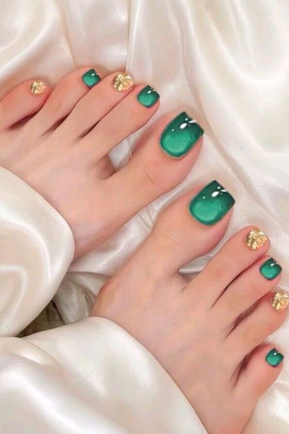 Close-up of bare feet with iridescent emerald green and gold pedicure designs, resting on white satin fabric.