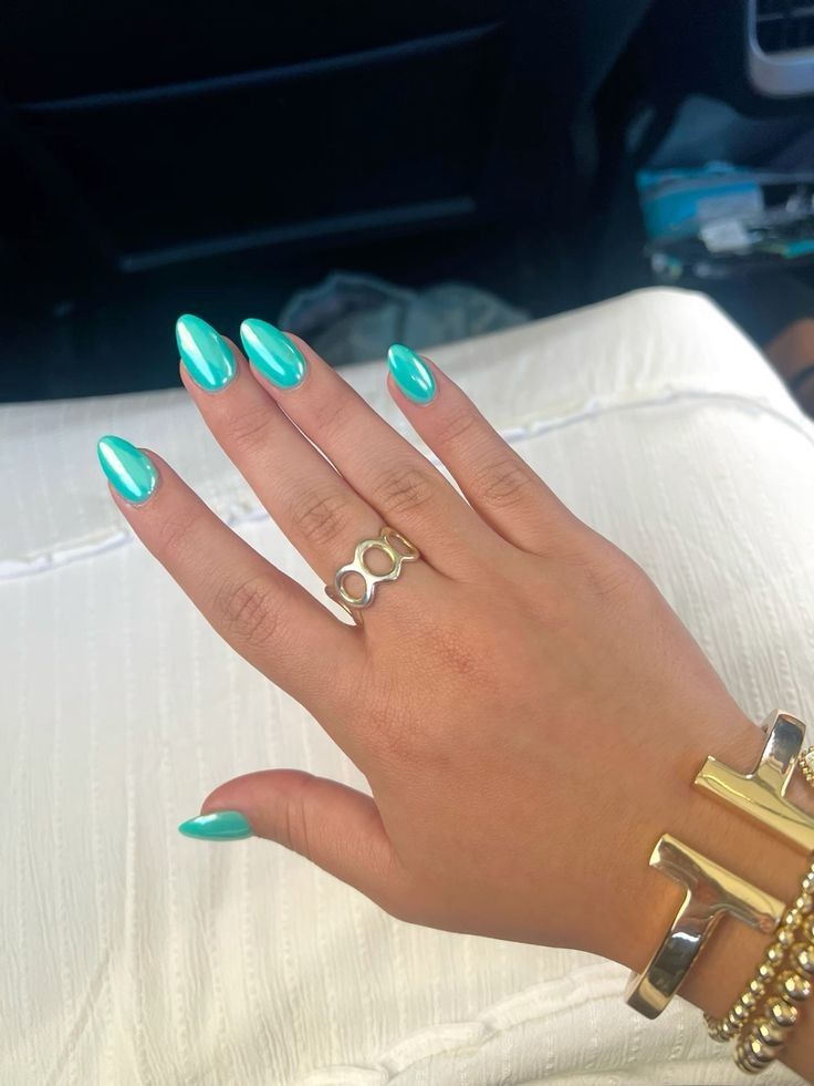 Hand with iridescent aqua almond-shaped nails, wearing a gold open-circle ring, and gold bracelets.