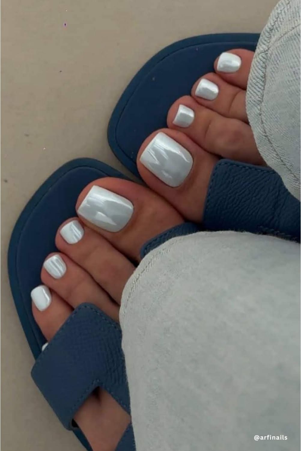Feet wearing blue sandals, with toes painted in an iridescent white polish.