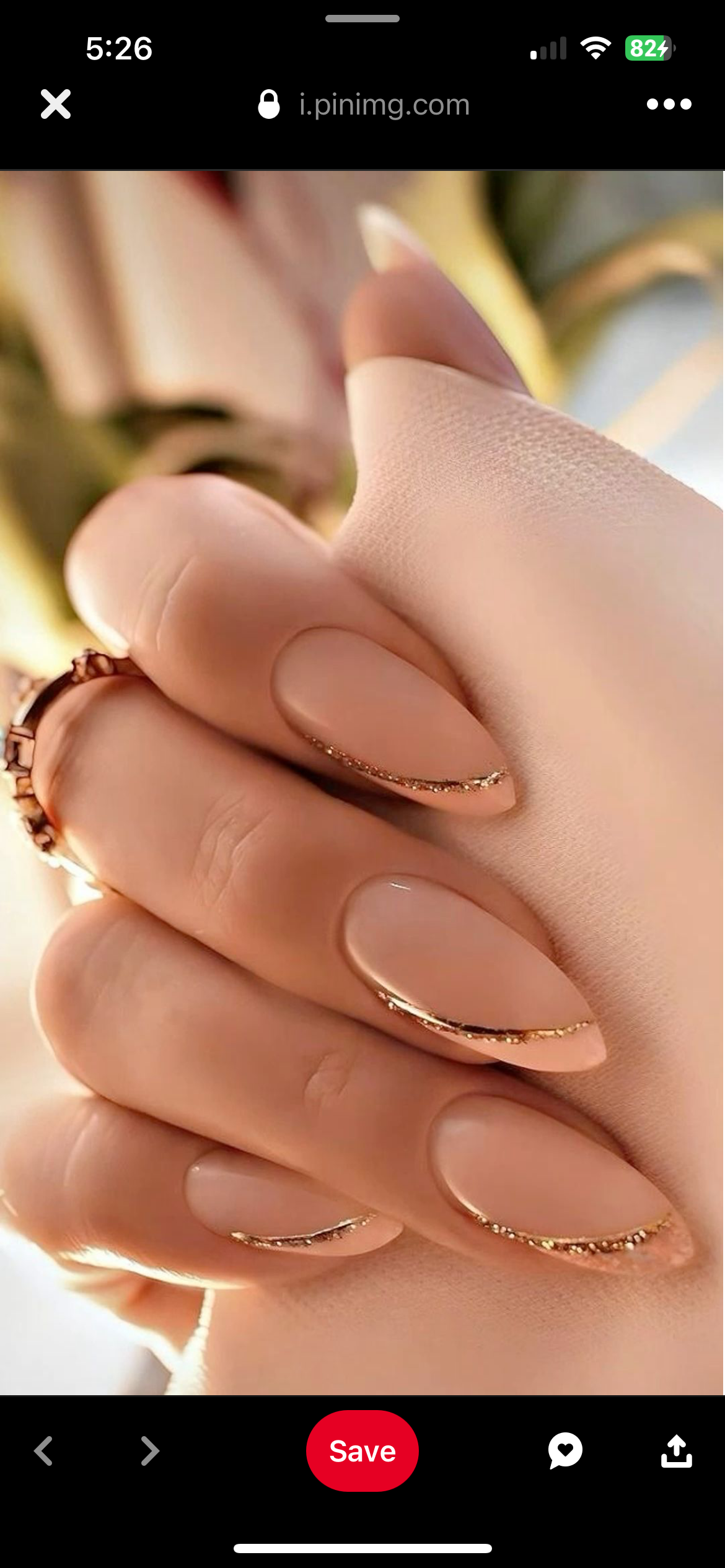 Close-up of a hand with almond-shaped nails in a warm nude color, featuring rose gold glitter French tips.
