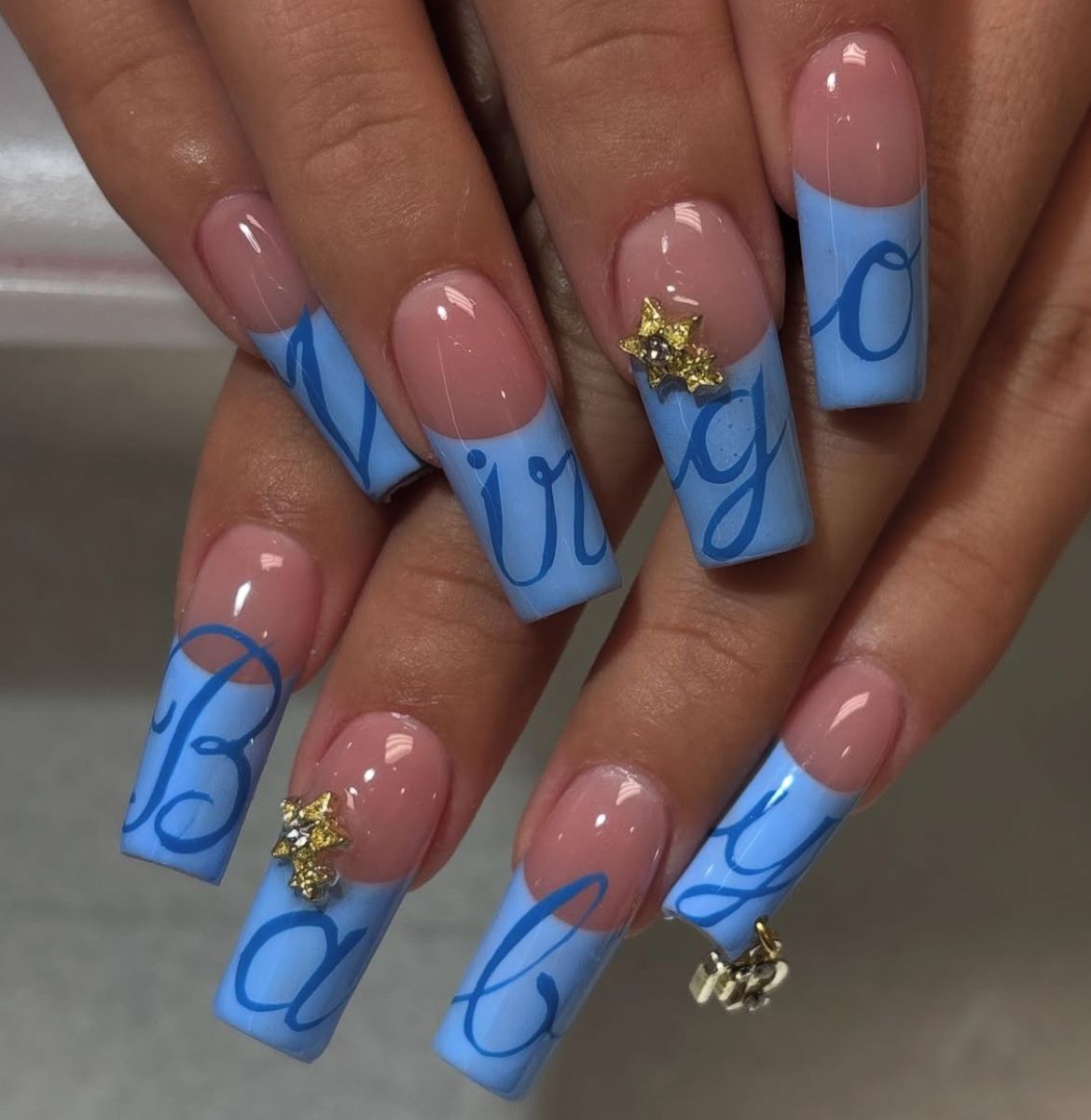Long, square-tipped nails feature a neutral pink base with light blue tips.