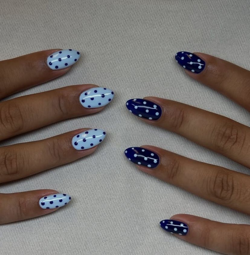 Close-up of fingers with almond-shaped nails, some painted pale blue with navy dots, others navy blue with white dots.