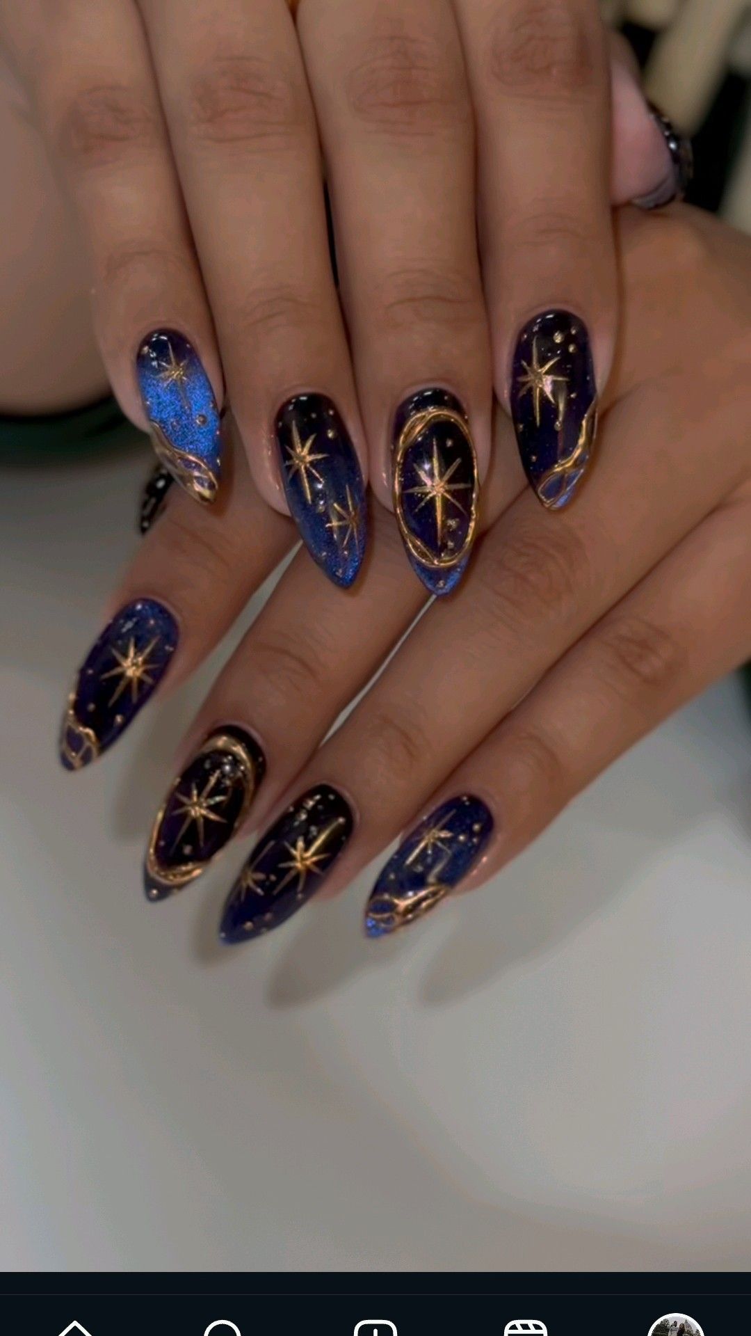 Close up of manicured hands with dark blue and lighter blue glitter nails, adorned with gold star and circular designs.