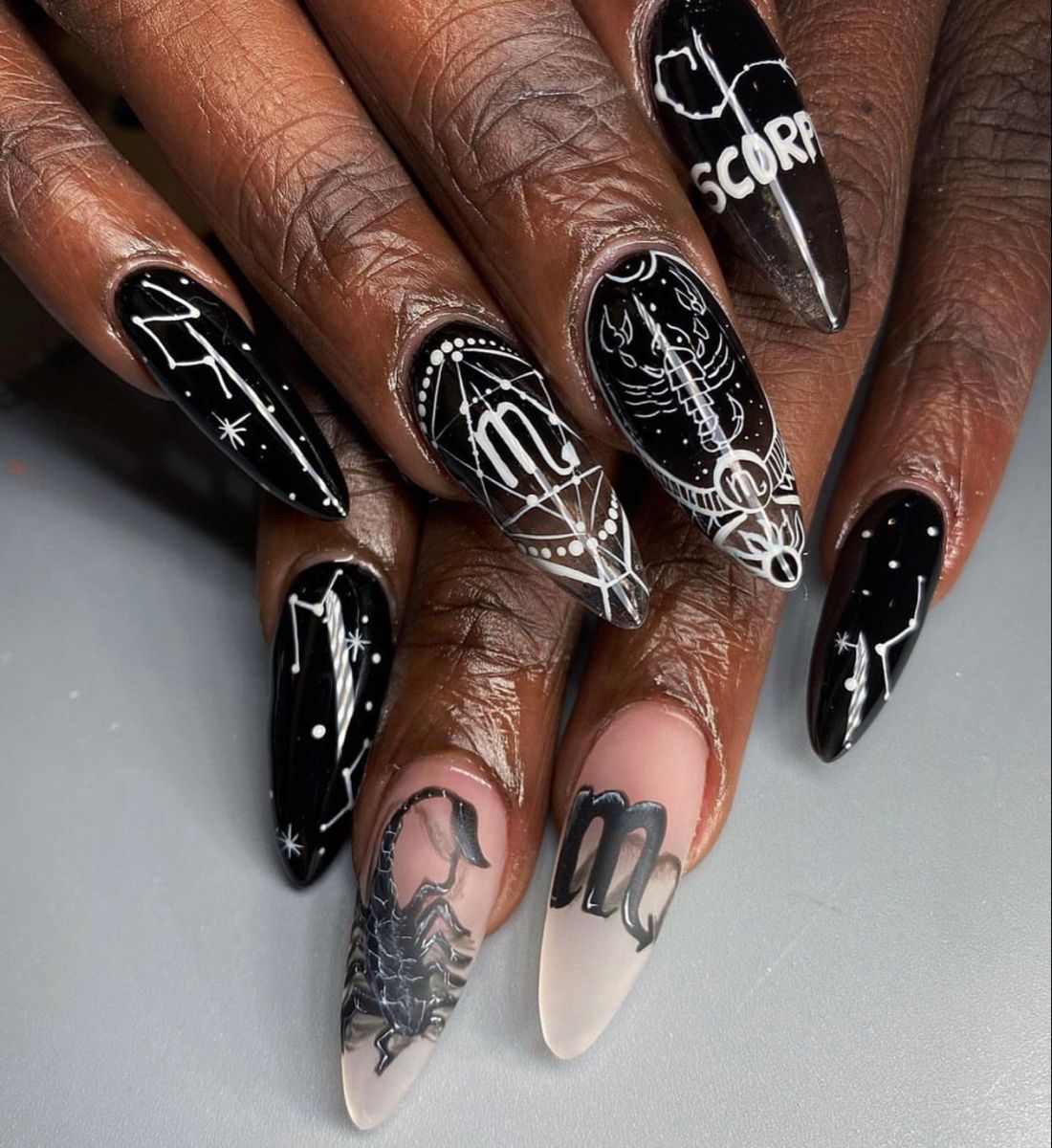 Close-up of manicured hands with long, almond-shaped nails featuring various black and white astrological designs.