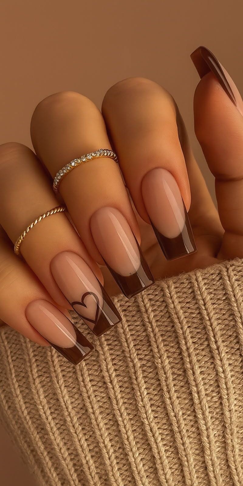 Hand with five coffin nails featuring brown French tips and a black outline heart on one nail.
