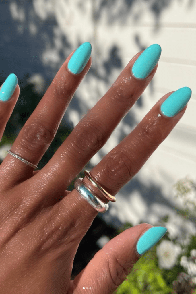 Close-up of a hand with five nails painted a solid aqua color, with one tiny rhinestone accent on a ring finger.