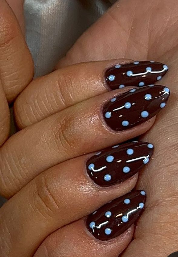 Close-up of fingers, each nail painted in a glossy dark brown with light blue polka dots.