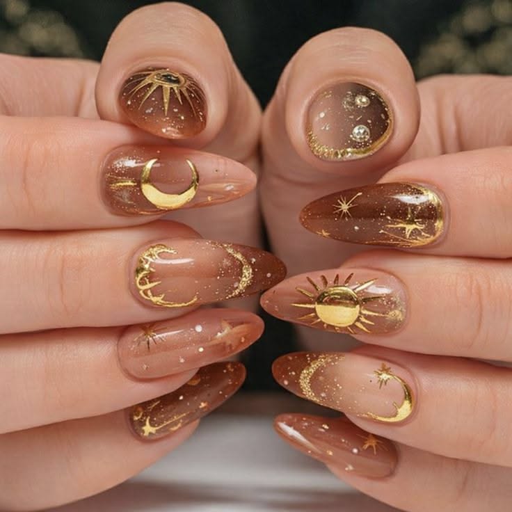 Close-up of hands with ten almond-shaped nails featuring brown ombré and gold celestial designs.