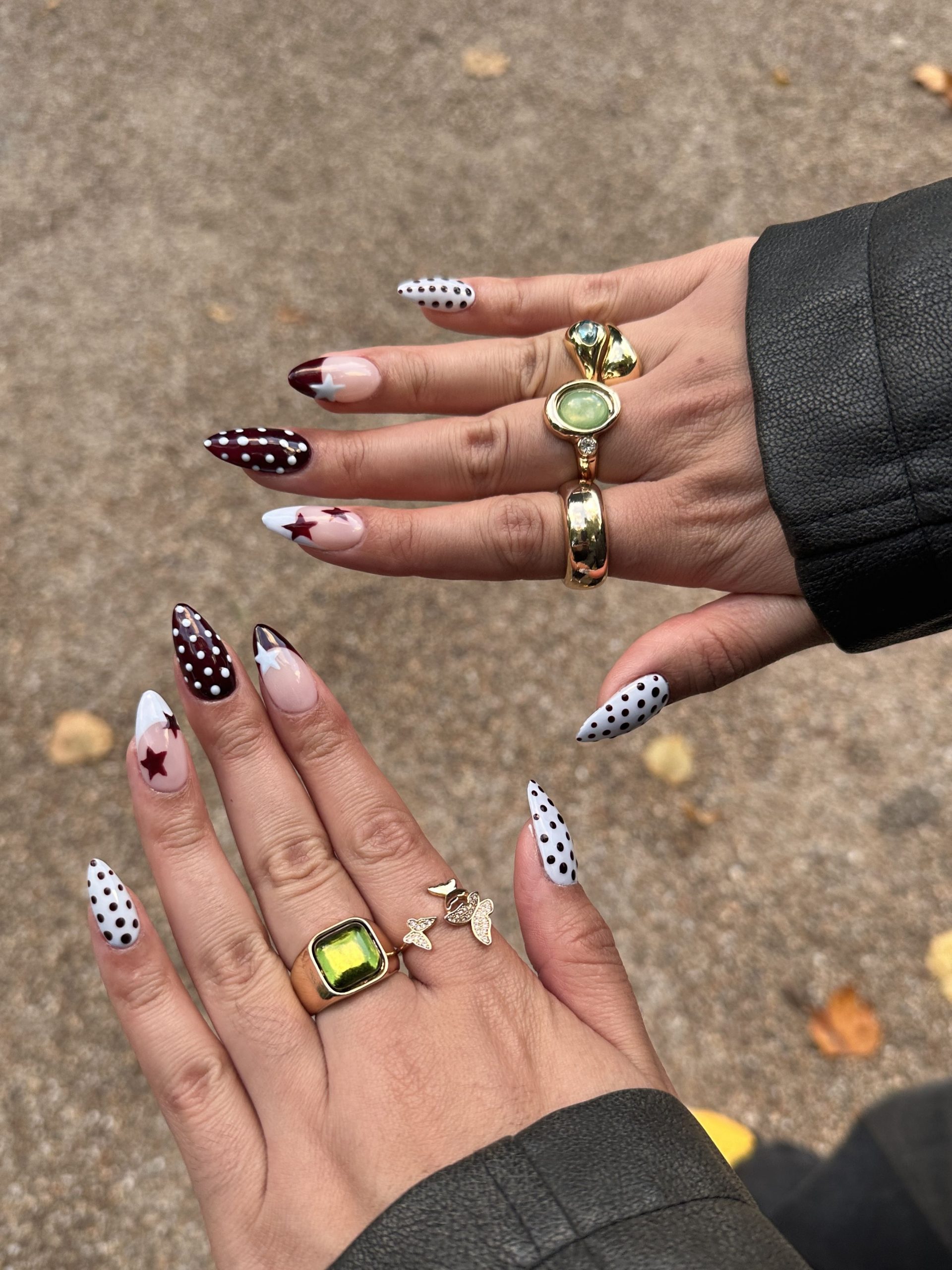 Close up on two hands with almond-shaped nails featuring white with small black polka dots, and a burgundy with a white star.