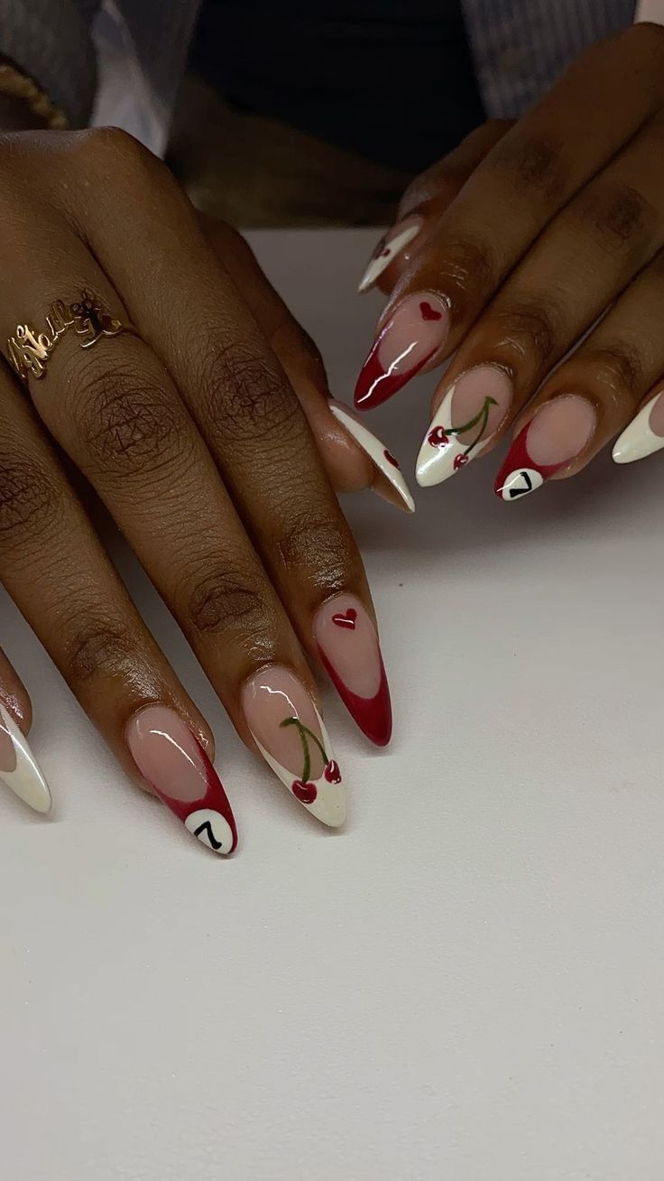 Close-up of manicured hands with long, red and white nails featuring hearts, cherries, and a number seven pool ball on some…