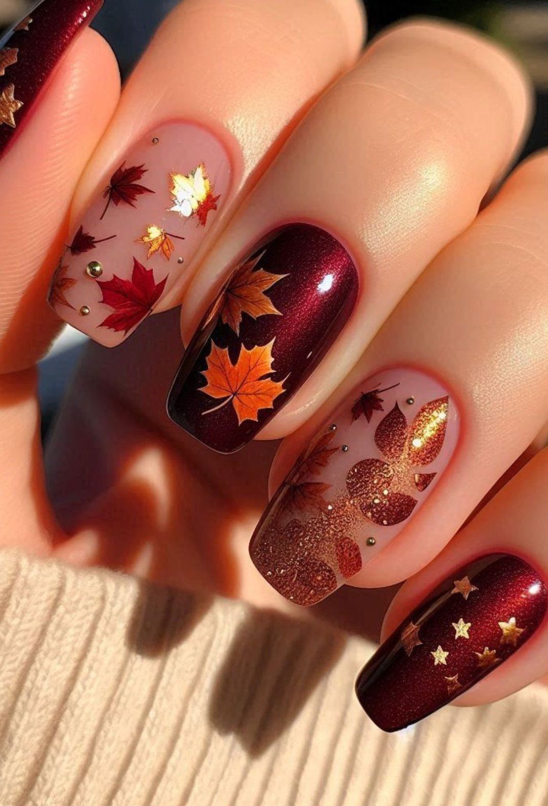 Close-up of manicured hand with acrylic nails, some feature detailed leaf designs and some feature glitter.