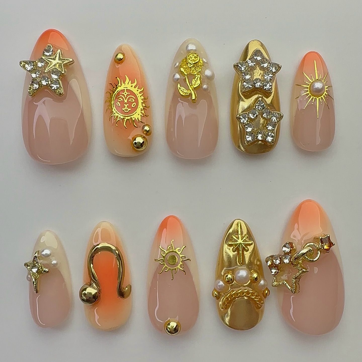 Set of ten almond-shaped press-on nails with an ombre peach and nude base, embellished with gold and diamante celestial…