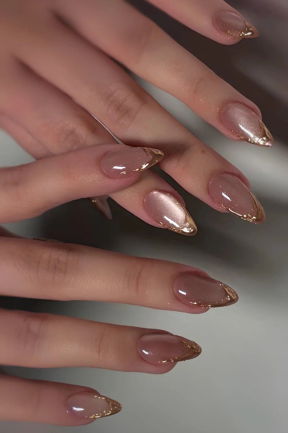 Almond-shaped nails with a nude base and gold metallic French tips.