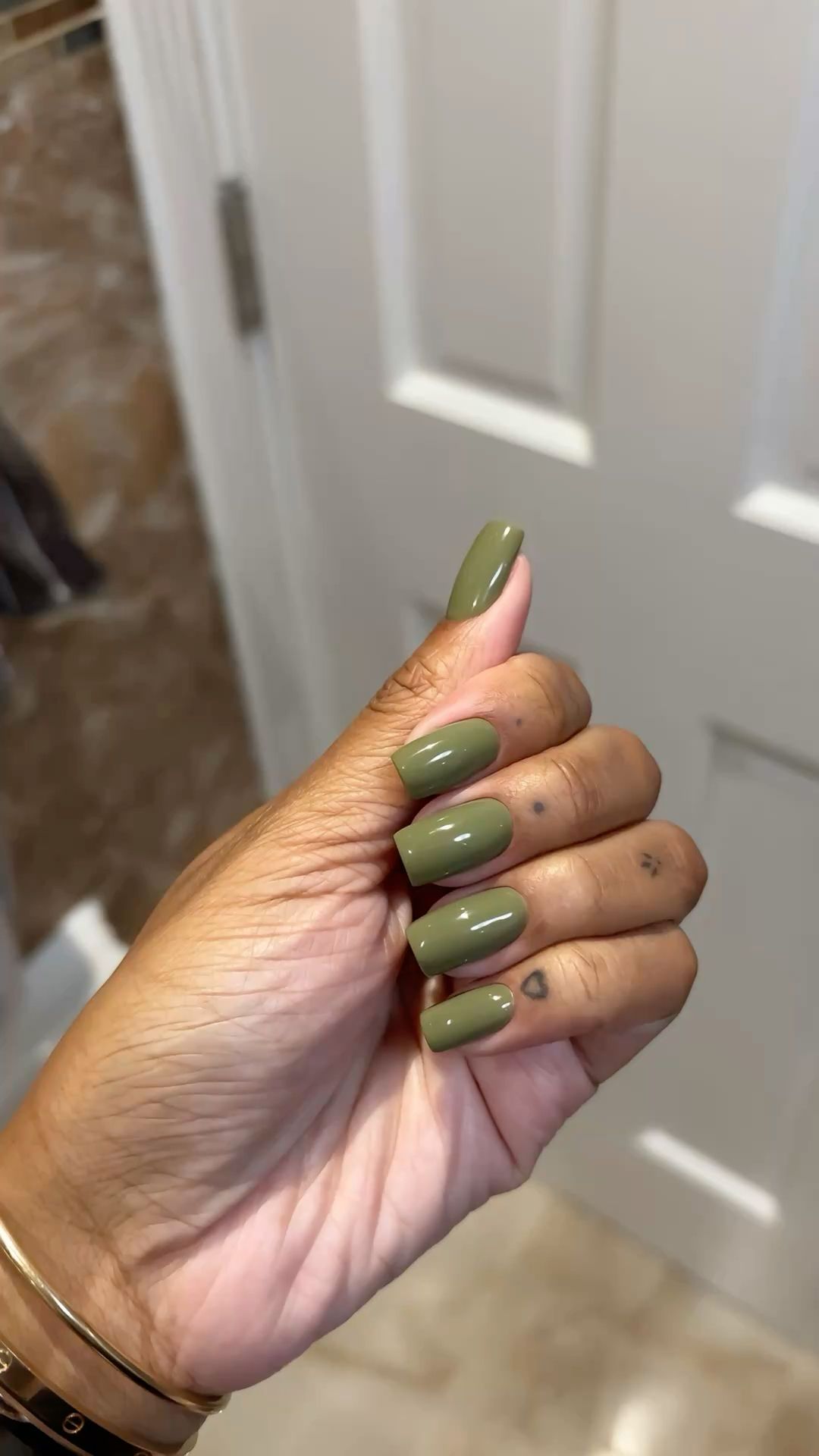 A hand with medium brown skin displays long, rectangular nails painted a solid military green color.