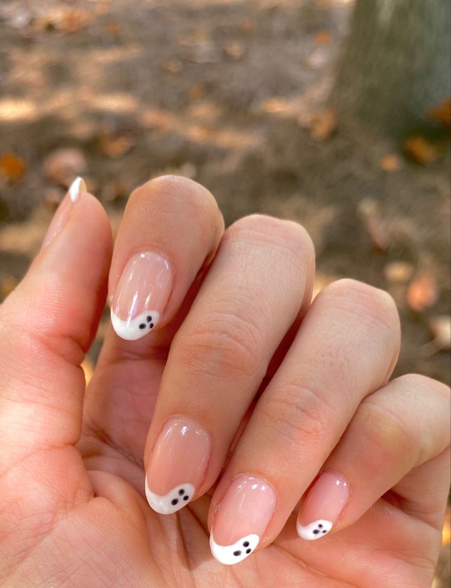 Close-up of a hand with short, clear French-tipped fingernails, each tip featuring a small, hand-drawn ghost design.