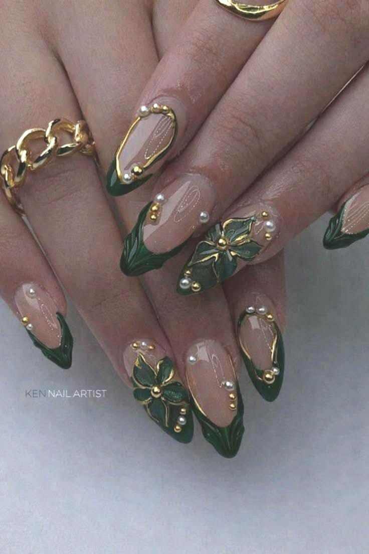 Pointed fingernails with military green and clear polish, adorned with gold accents and small white pearls.