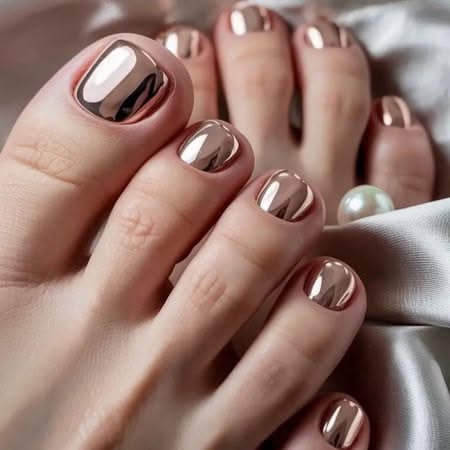Close up of feet with rose gold metallic polished toenails, resting on a white fabric with a pearl bead.